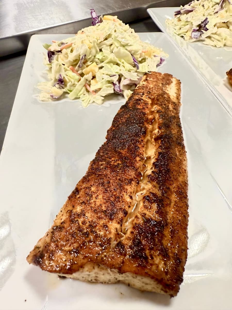 A spice-crusted grilled mahi fillet on a white plate beside a mound of mango wasabi slaw